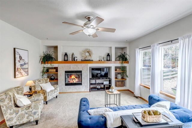 carpeted living room with a tiled fireplace, baseboards, and ceiling fan