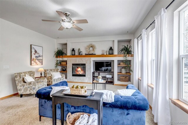 carpeted living area with a ceiling fan, baseboards, a tiled fireplace, and a wealth of natural light