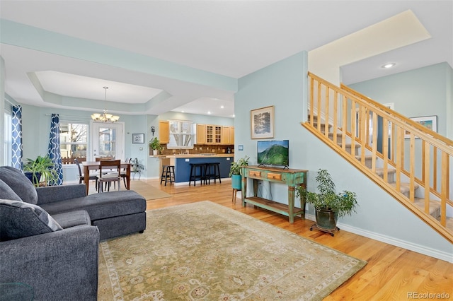 living room with baseboards, a raised ceiling, wood finished floors, stairs, and a chandelier