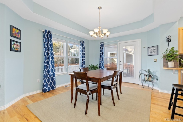 dining room with light wood finished floors, a raised ceiling, and baseboards