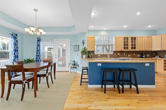 kitchen with a breakfast bar, light wood-style floors, decorative backsplash, light brown cabinetry, and glass insert cabinets