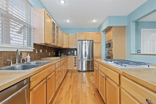 kitchen featuring appliances with stainless steel finishes, light countertops, a sink, and light brown cabinetry