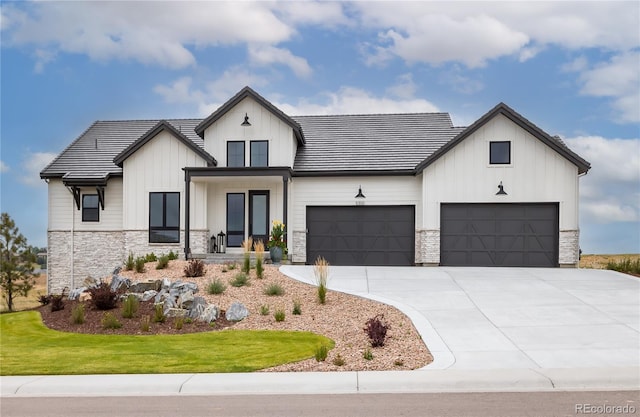 modern farmhouse style home featuring a front yard, concrete driveway, a garage, stone siding, and board and batten siding