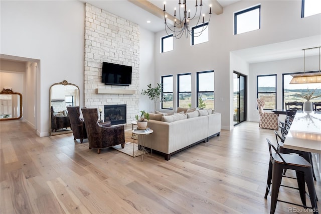 living room with light wood-type flooring, a towering ceiling, a stone fireplace, and a chandelier