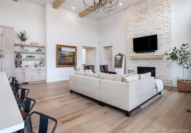 living room with light hardwood / wood-style flooring, a chandelier, a towering ceiling, beam ceiling, and a fireplace