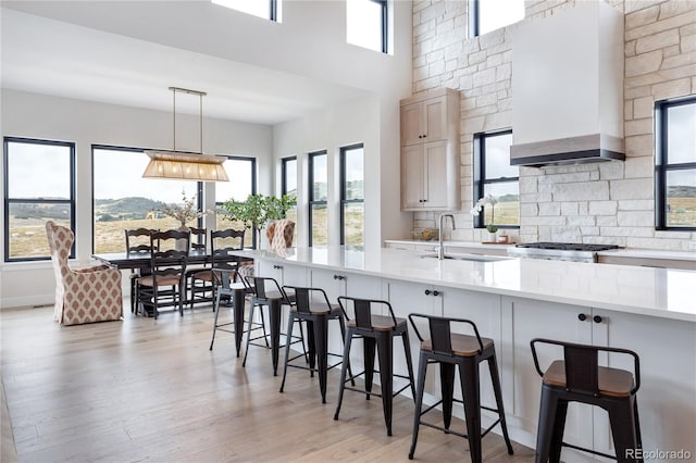 kitchen with custom range hood, light hardwood / wood-style floors, sink, decorative light fixtures, and a breakfast bar area