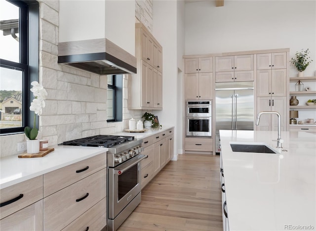 kitchen with sink, light wood-type flooring, light brown cabinetry, wall chimney range hood, and premium appliances