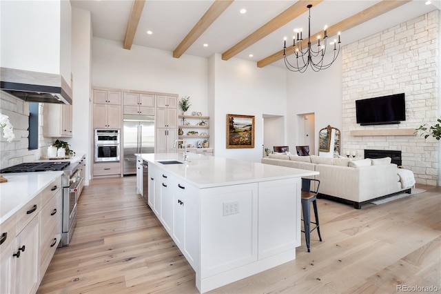 kitchen featuring wall chimney range hood, light hardwood / wood-style floors, an inviting chandelier, a center island with sink, and high end appliances