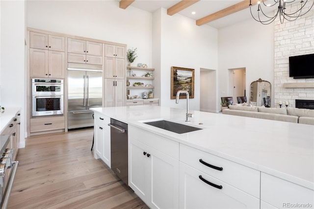 kitchen with sink, a fireplace, beamed ceiling, appliances with stainless steel finishes, and light wood-type flooring