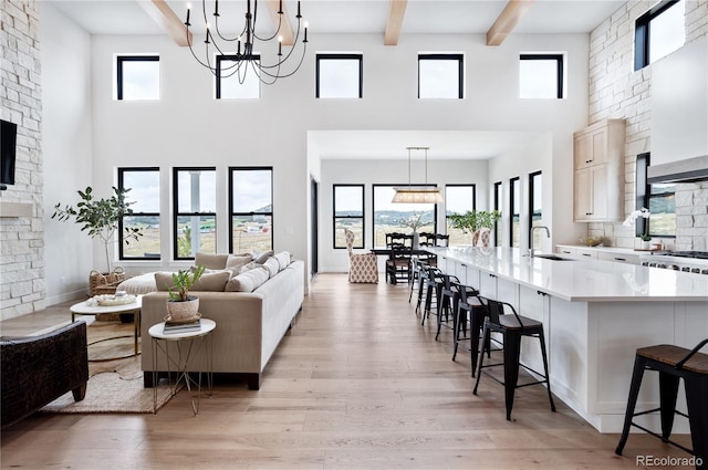 living room with a high ceiling, sink, beamed ceiling, light wood-type flooring, and a notable chandelier