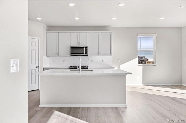 kitchen featuring a center island with sink, light wood-type flooring, and backsplash