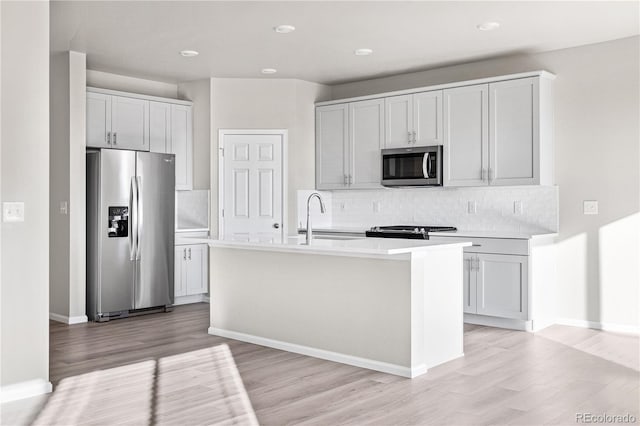 kitchen featuring appliances with stainless steel finishes, an island with sink, light hardwood / wood-style floors, and sink