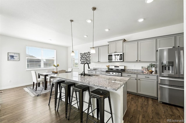 226 Racer St, Bennett, CO 80102 - kitchen with appliances with stainless steel finishes, gray cabinetry, a breakfast bar, light stone countertops, and a kitchen island with sink