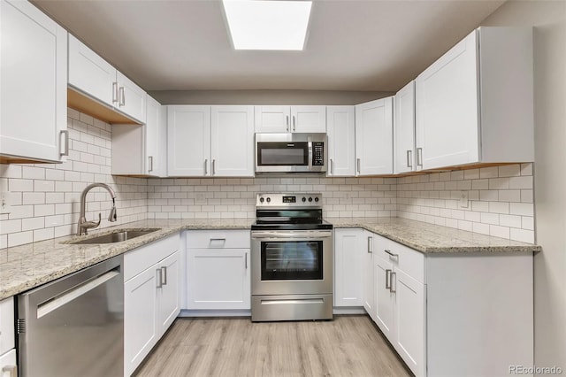 kitchen with white cabinets, sink, tasteful backsplash, stainless steel appliances, and light hardwood / wood-style floors