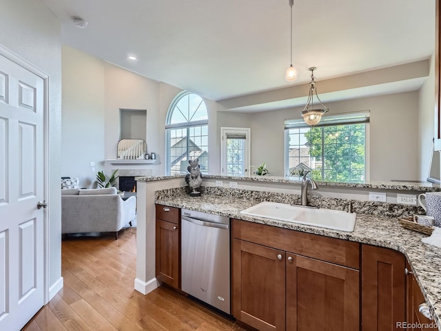6827 S Webster St Unit E, Littleton, CO 80128 - kitchen featuring stainless steel dishwasher, light wood-type flooring, hanging light fixtures, a warm lit fireplace, and light stone countertops