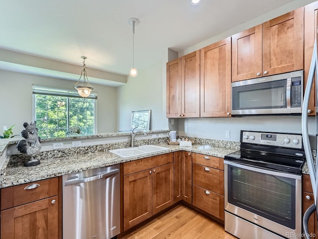 6827 S Webster St Unit E, Littleton, CO 80128 - kitchen with stainless steel appliances, light wood-style flooring, hanging light fixtures, light stone countertops, and brown cabinetry