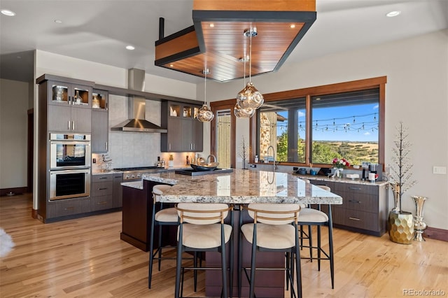 kitchen featuring stainless steel appliances, light hardwood / wood-style floors, wall chimney range hood, and decorative light fixtures