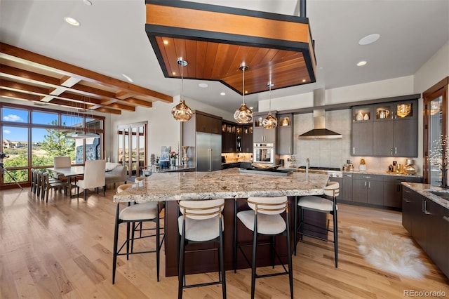 kitchen featuring dark brown cabinets, appliances with stainless steel finishes, light hardwood / wood-style floors, and wall chimney range hood