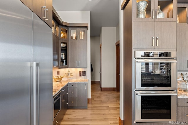 kitchen with appliances with stainless steel finishes, backsplash, light stone countertops, and light hardwood / wood-style flooring