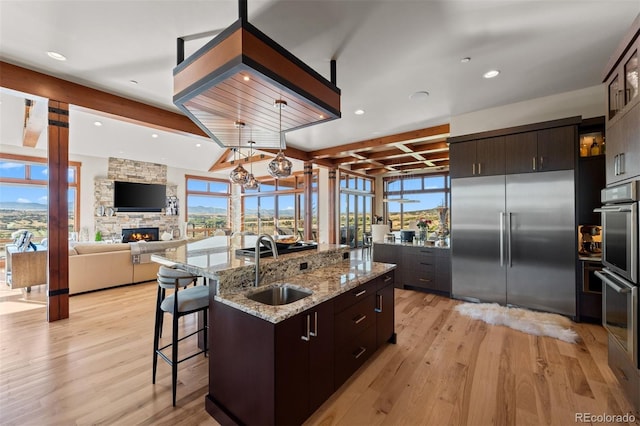 kitchen with dark brown cabinetry, appliances with stainless steel finishes, a large island with sink, and a wealth of natural light