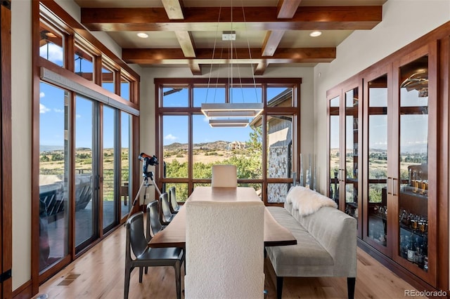 dining area featuring a notable chandelier, light hardwood / wood-style floors, beamed ceiling, and a healthy amount of sunlight