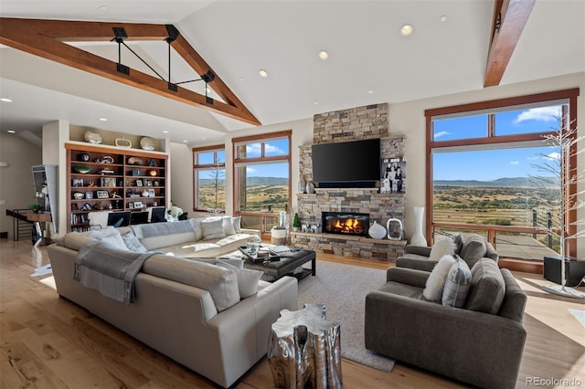 living room featuring a stone fireplace, beamed ceiling, light hardwood / wood-style flooring, and high vaulted ceiling