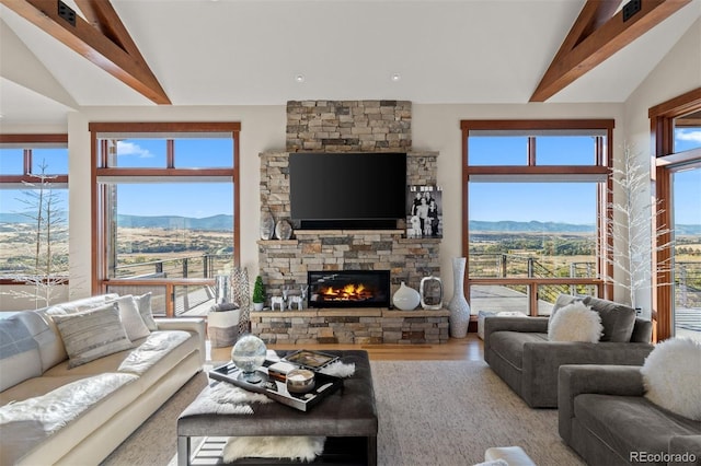 living room featuring wood-type flooring, a stone fireplace, and lofted ceiling with beams