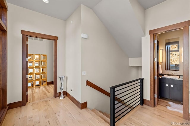 hall with light wood-type flooring, lofted ceiling, and sink