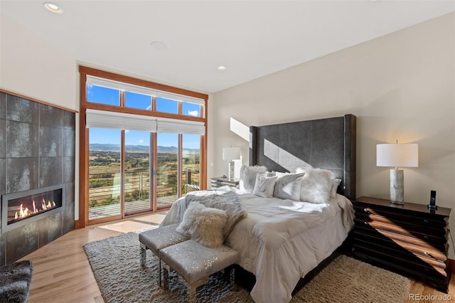 bedroom with access to outside, a fireplace, and light wood-type flooring