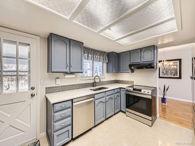 kitchen with appliances with stainless steel finishes, gray cabinets, light countertops, under cabinet range hood, and a sink