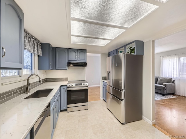 kitchen featuring stainless steel appliances, a healthy amount of sunlight, a sink, light stone countertops, and under cabinet range hood