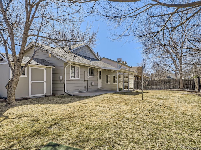 rear view of property featuring an outbuilding, fence, a yard, roof with shingles, and a patio area