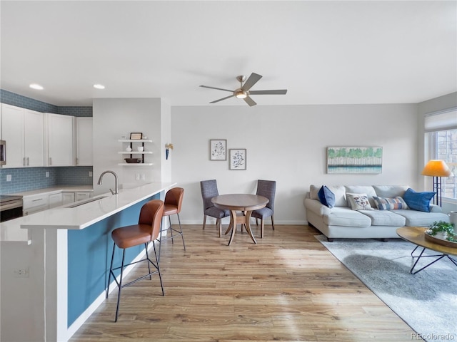 kitchen with white cabinetry, sink, a kitchen bar, light hardwood / wood-style floors, and kitchen peninsula