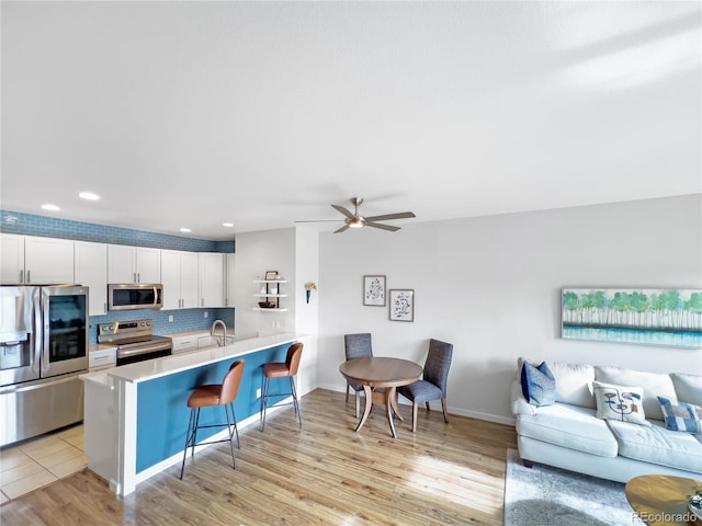 kitchen featuring appliances with stainless steel finishes, a breakfast bar, white cabinetry, sink, and kitchen peninsula