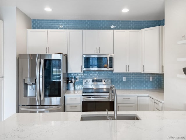 kitchen featuring stainless steel appliances, light stone countertops, sink, and white cabinets