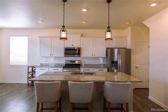 kitchen with a kitchen island with sink, dark hardwood / wood-style flooring, sink, decorative backsplash, and appliances with stainless steel finishes