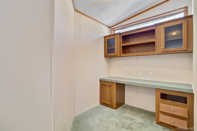 unfurnished office featuring vaulted ceiling, built in desk, light colored carpet, and a textured ceiling