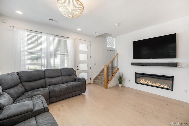 living area featuring stairs, a glass covered fireplace, a healthy amount of sunlight, and light wood-style flooring