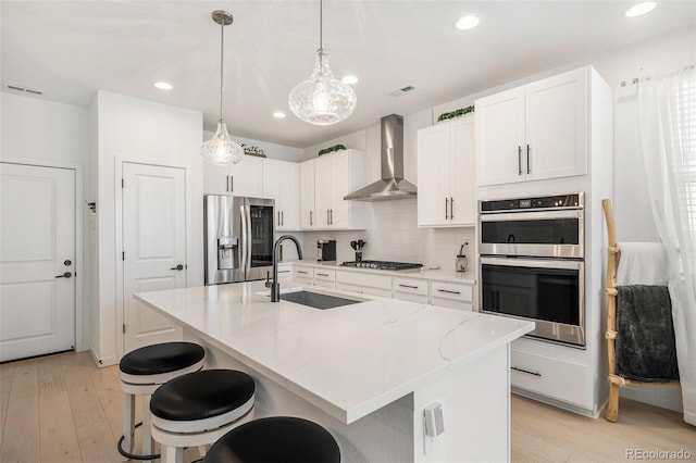 kitchen with visible vents, light wood-style floors, wall chimney range hood, a sink, and appliances with stainless steel finishes