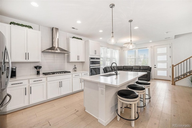 kitchen with visible vents, wall chimney range hood, a sink, light wood-style flooring, and stainless steel appliances