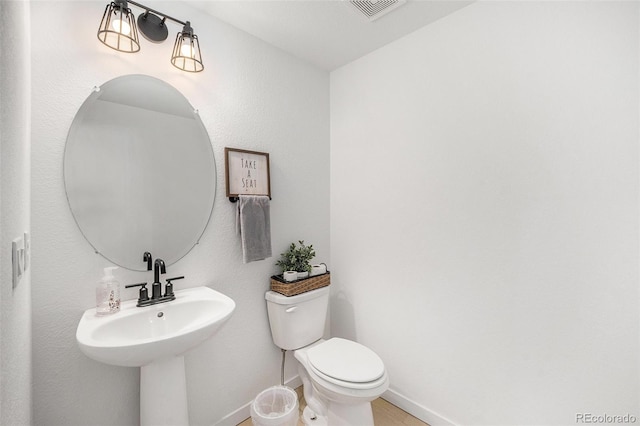half bathroom featuring a sink, baseboards, toilet, and visible vents