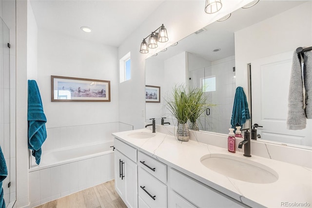 full bath with double vanity, a shower stall, a sink, and wood finished floors