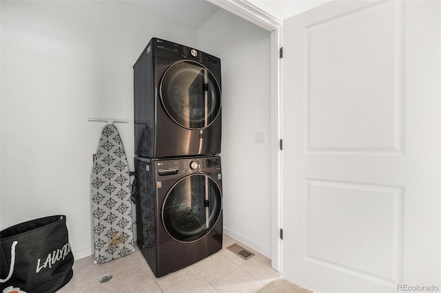 washroom with laundry area, stacked washer and dryer, visible vents, light tile patterned flooring, and baseboards