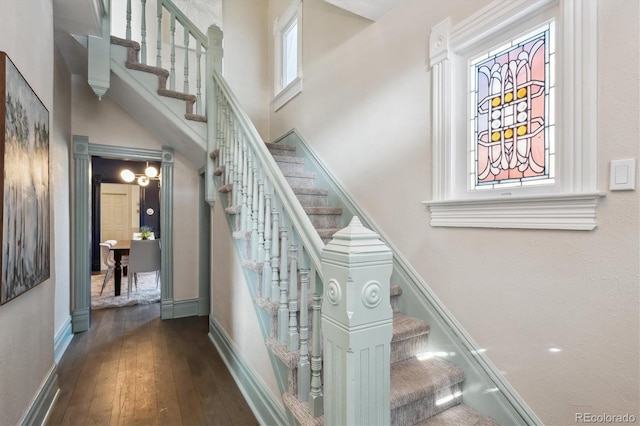 stairway featuring a towering ceiling, baseboards, and wood finished floors