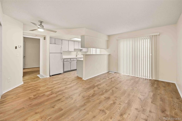 unfurnished living room featuring ceiling fan, sink, a textured ceiling, and light wood-type flooring