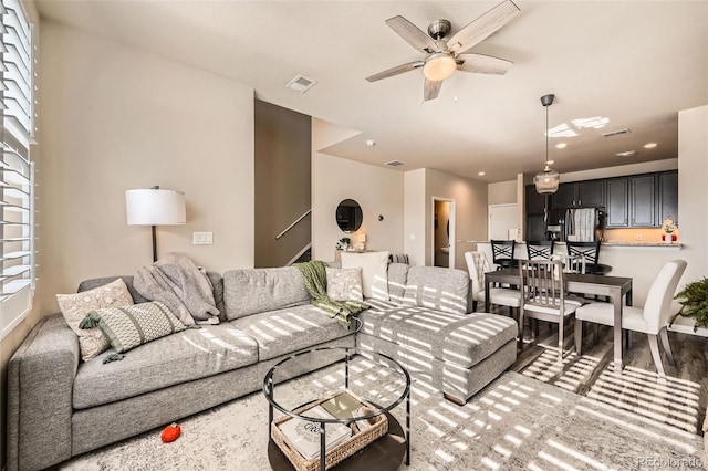 living area with visible vents, light wood-style flooring, stairs, and ceiling fan