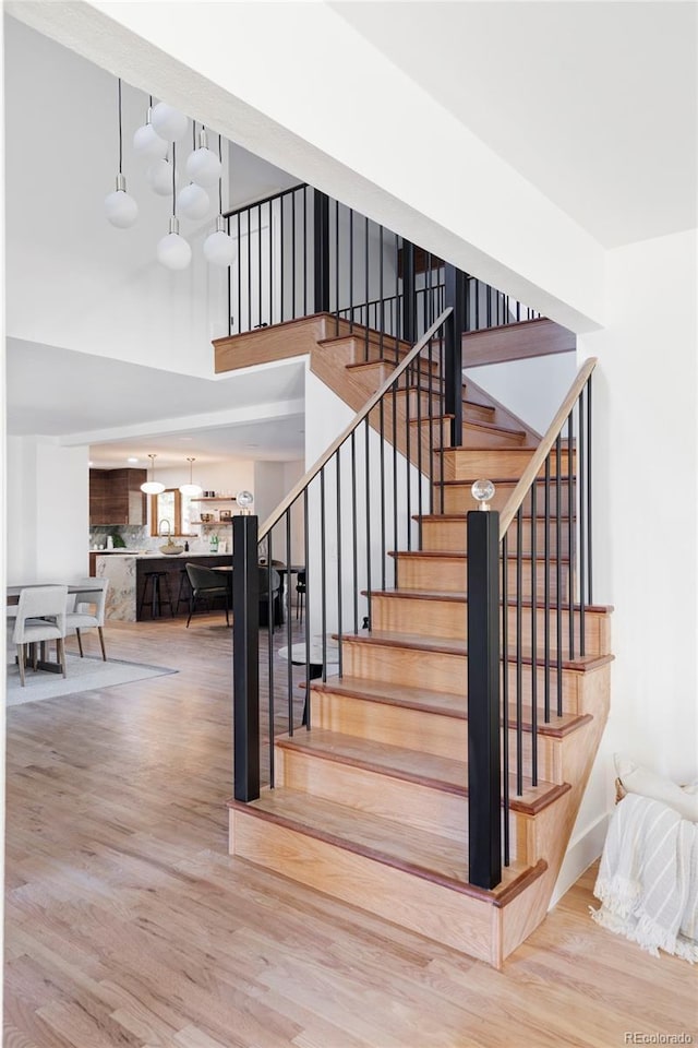 stairs with a high ceiling, wood finished floors, and an inviting chandelier