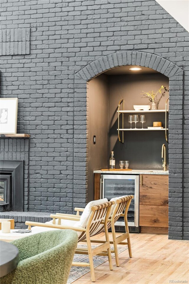 bar with beverage cooler, wood finished floors, indoor bar, a fireplace, and brick wall