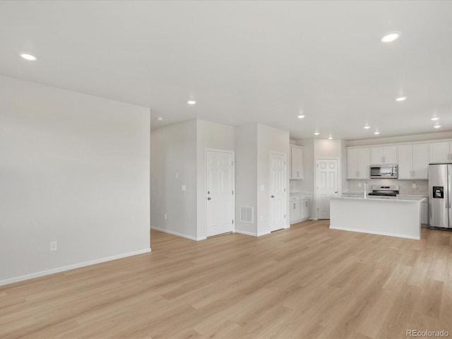 unfurnished living room with light wood finished floors, baseboards, recessed lighting, and a sink