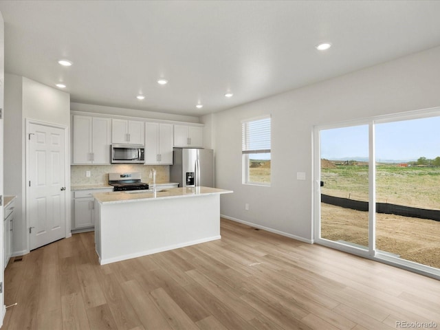 kitchen with appliances with stainless steel finishes, light countertops, a center island with sink, light wood-style flooring, and recessed lighting